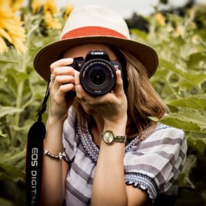 Woman with hat photographing sunflowers in a summer field using a Canon camera.